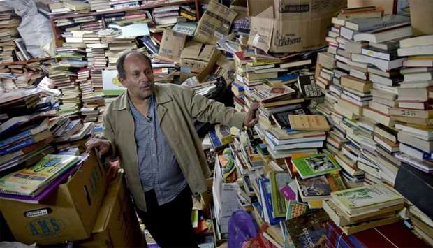 Jose Alberto Gutierrez checks books stacked in his library on the first floor of his house in Bogota