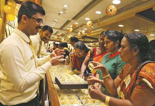 A salesman shows gold bangles to customers inside a jewellery showroom on the  occasion of Akshaya Tritiya, a major gold buying festival, in Kochi. Indiau2019s this yearu2019s gold imports are likely to be 725 tonnes, according to a Reuters poll.