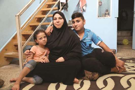 Syrian refugee Mounir (right, name changed), his mother Hasnaa, and six-year-old sister (left) sit in their house which was once a garage in Tripoli, Lebanon.