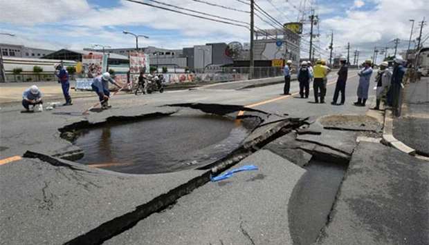 Workers stand by a partially collapsed road following an earthquake in Takatsuki, north of Osaka prefecture, on Monday.