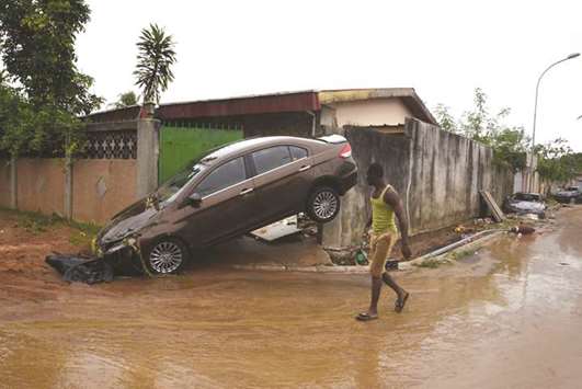 A pedestrian walks past the wreckage of a vehicle on a street in Abidjan yesterday after floodwaters receded following an overnight downpour in the city.