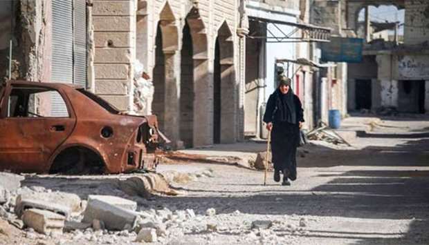 A woman walks with a cane past a destroyed car in Al-Hirak in the eastern Deraa province on Thursday.