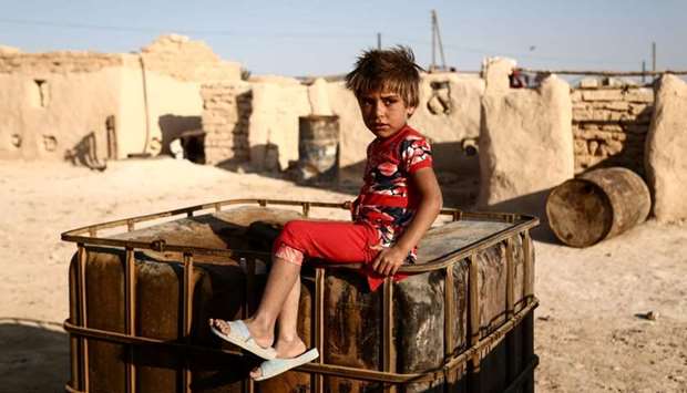 A Syrian child from the northern city of Manbij, displaced by fighting between the Syrian Democratic Forces (SDF) and Islamic State (IS) group fighters, sits outside mud-brick dwellings at Al-Qadi camp for the displaced.