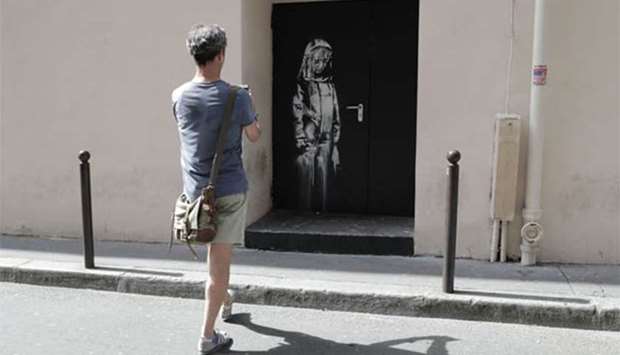 A man takes a photograph of a recent artwork by street artist Banksy in Paris on Monday.