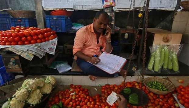 A vendor speaks on his mobile phone as he maintains his ledger book at a stall selling vegetables in Mumbai on Monday.