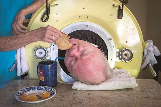 FOOD FOR THOUGHT: Caregiver and friend Kathryn Gaines feeds toast to Paul Alexander inside his iron lung at his home in Dallas. Below, Alexander chats with Gaines as he drinks coffee.