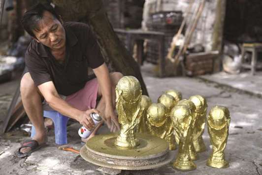 Craftsman Vuong Hong Nhat spraying gold colour paint on a plaster model of the football World Cup trophy at a workshop in Hanoi.