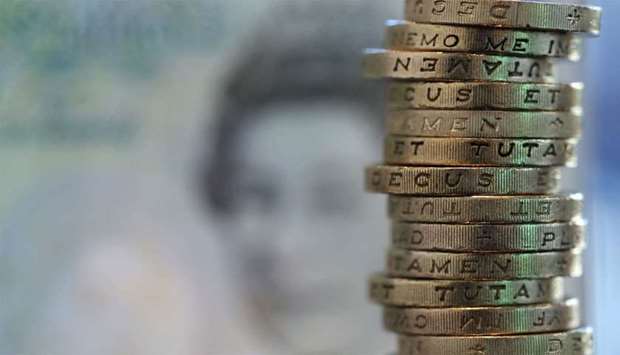 British one pound coins stand stacked near the printed face of Queen Elizabeth II on a five pound note