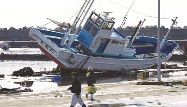 People walk past a ship run aground at Oarai Port after an earthquake in Oarai town, Ibaraki prefecture, Japan, in this March 12, 2011 file picture.