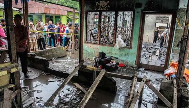 Onlookers gather in front of a burnt-out house that doubled as a matchstick factory in Binjai.