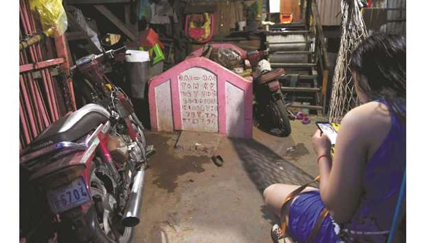 A woman looking at her smartphone beside a grave inside her home in Phnom Penh.