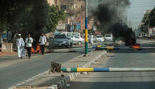People walk past burning tires after protesters set fire and pulled down street light polls on a street, in the capital Khartoum's twin city Omdurman
