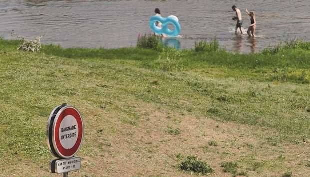 A sign reads u2018Bathing prohibitedu2019 as people wade through the water of the Loire River in Tours, France.