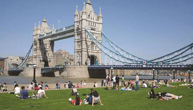 This file photo shows people relaxing in hot and sunny weather on the grass beside the Tower Bridge and the river Thames in London. Londonu2019s iconic Tower Bridge celebrates its 125th anniversary today by showing off the weird and wacky alternative designs that were nearly built instead.