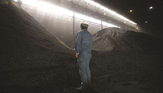 An employee stands in front of stockpiles of coal inside a storage yard at a coal fired power station in Japan.