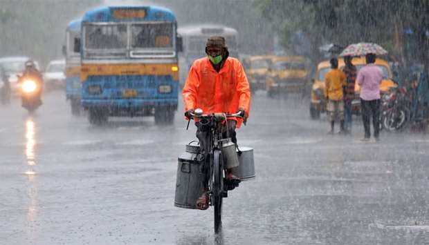 A milk vendor wearing a protective face mask rides his bicycle during heavy rain, after authorities eased lockdown restrictions that were imposed to slow the spread of the coronavirus disease, in Kolkata, India