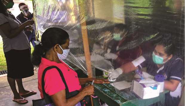 A Sri Lankan election official behind a plastic sheet marks the finger of a voter (second left) with ink during a mock election to test the guidelines implemented against the coronavirus in Ingiriya of Kalutara District in Western Province yesterday.