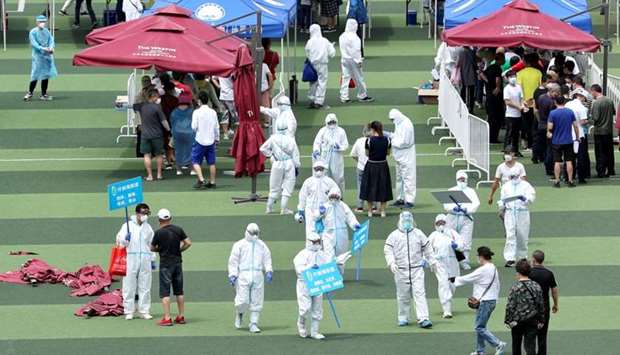 Medical workers in protective suits help people lining up inside a sports centre for nucleic acid tests, following new cases of coronavirus disease infections in Beijing