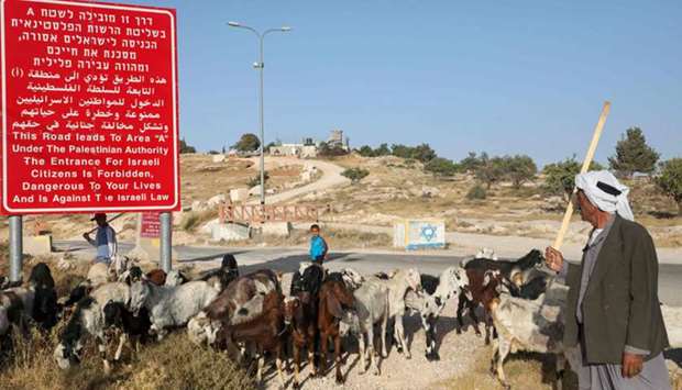 A Palestinian shepherd leads his flock of sheep past a sign, which signals the start of Zone A which is under Palestinian Authority and is forbidden for Israeli citizens, near the town of Bani Naim, east of the town of Hebron in the occupied West Bank and north of the settlement of Maale Hever, yesterday.