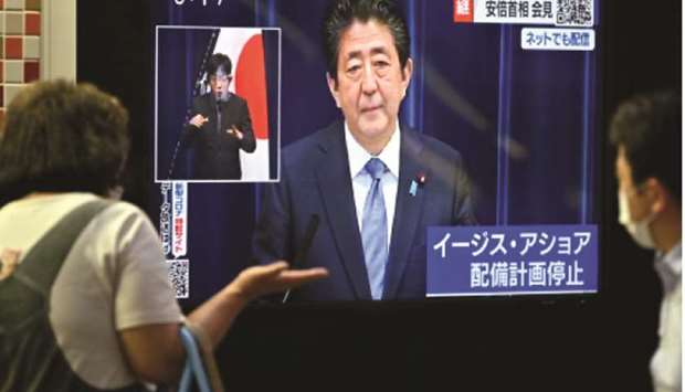 Pedestrians walk past as a television screen showing a broadcast of Japanese Prime Minister Shinzo Abe speaking during a press conference in Tokyo yesterday.