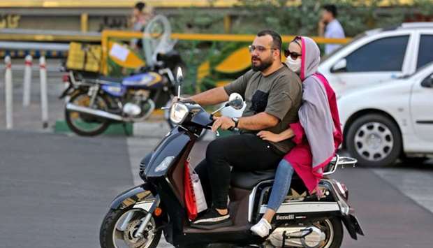 An Iranian woman wearing a face mask rides on the back of a motorcycle in Tehran