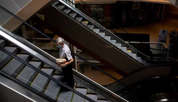 A elderly man wearing a protective mask carries a take-away bag as he rides an escalator inside a shopping mall, which has reopened after two months as lockdown restrictions ease amid the coronavirus disease