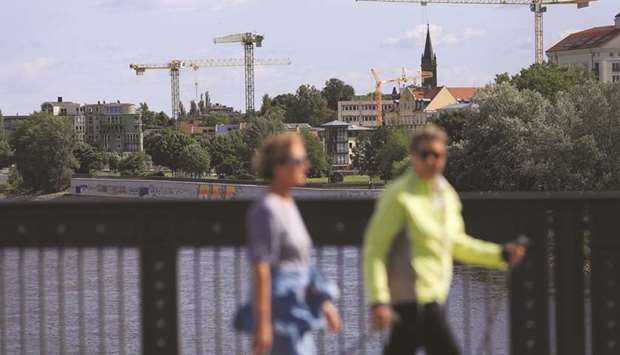 Construction cranes stand near the River Elbe as pedestrians cross the Zollbruecke bridge in Magdeburg, Germany. Officials in Germany are now focusing on trying to bring the economy back from a contraction expected to exceed 6% this year, the deepest since the aftermath of World War II.