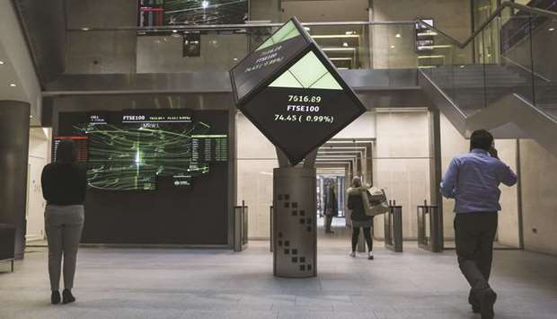 Employees walk past FTSE100 share price information displayed on an illuminated rotating cube in the atrium of the London Stock Exchange. Most UK stock market participants want a reduction in the worldu2019s longest trading hours, which they say can improve liquidity and industry diversity, according to the results of a LSE survey.