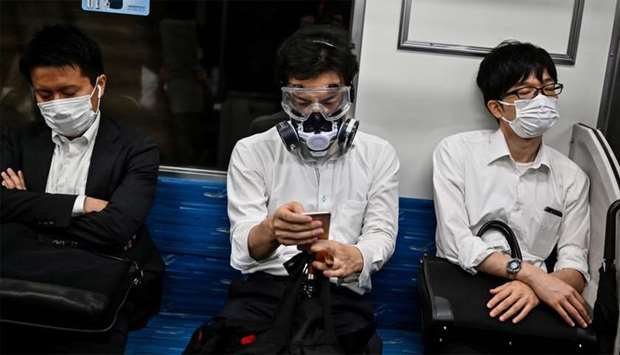 A man wearing a respirator and googles sits in between facemask-clad commuters in a train in Tokyo