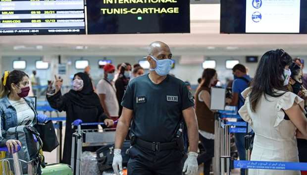 A mask-clad member of Tunisia's Rapid Intervention Brigade (BIR) walks past passengers queueing to check-in their luggage before boarding departing flights at Tunis-Carthage International Airport in the Tunisian capital on June 27, 2020, as the North African country re-opens its land, sea, and air borders following a four-month closure due to the coronavirus pandemic