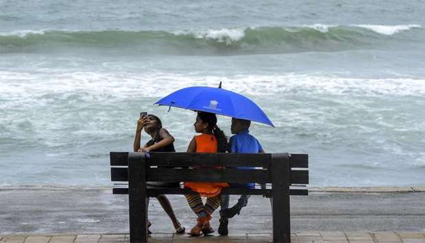 Children take shelter under an umbrella as they sit on a bench facing the sea along the coast during a downpour in Colombo