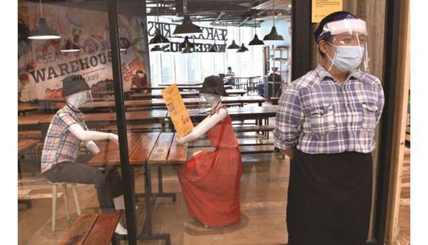 A staff member of a restaurant stands near mannequins wearing face masks and face shields displayed inside a restaurant, to simulate seating arrangements when restaurants will be allowed to once again cater to dine-in customers, in a mall in Manila.