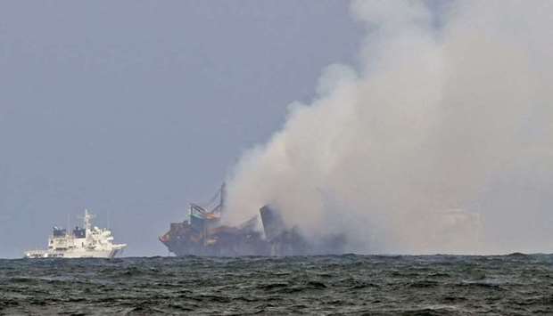 An Indian Coast Guard ship (L) tries to douse off the fire as smoke billows from the Singapore-registered container ship MV X-Press Pearl, which has been burning for the 12th consecutive day in the sea off Sri Lanka's Colombo Harbour, on a beach in Colombo yesterday.