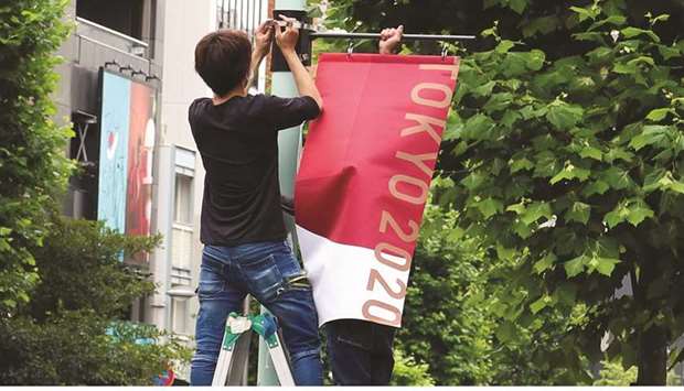 Workers attach the Tokyo 2020 Olympic Games banner on a lamp post in Tokyo, Japan, yesterday. (Reuters)