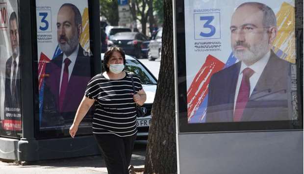 A woman wearing a face mask walks past campaign banners of acting Prime Minister Nikol Pashinian in Yerevan as Armenians vote on June 20, in snap parliamentary elections called by Prime Minister Nikol Pashinyan to end a political crisis