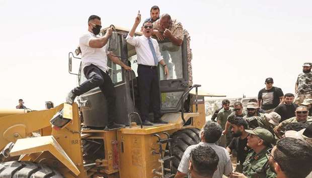 Libyan interim Prime Minister Abdulhamid Dbeibah, waves as he stands atop an excavator in the town of Buwairat al-Hassoun, during a ceremony to mark the reopening of 300km road between the cities of Misrata and Sirte.