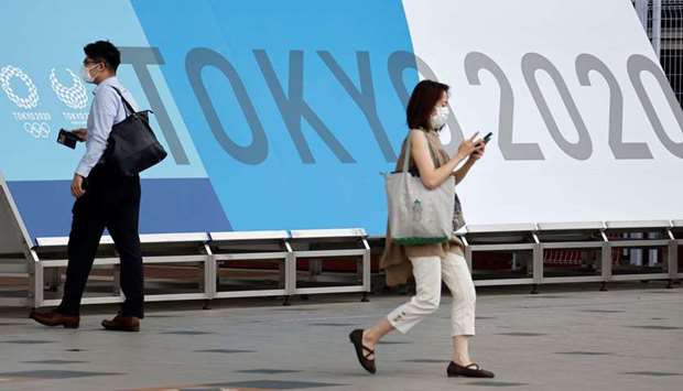 People walk past a sign for the 2020 Tokyo Olympic Games that have been postponed to 2021 due to the coronavirus disease (Covid-19) pandemic, at the IBC/MPC media center at Tokyo Big Sight exhibition center in Tokyo, Japan