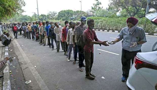 Homeless people mostly working as daily wage labourers, out of jobs due to COVID-19 coronavirus, queue up as a volunteer distributes food along the roadside in New Delhi, India. (AFP)