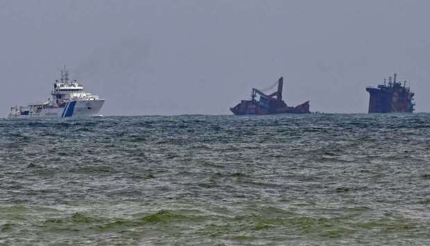 An Indian Coast Guard ship (L) approaches near the Singapore-registered container ship MV X-Press Pearl that partially sunk after burning for almost two weeks, just outside Colombo's harbour, as foreign experts have been deployed to help Sri Lanka contain a potential oil leak from the burnt-out container ship. AFP