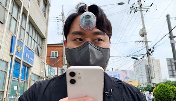 South Korean industrial designer Paeng Min-wook showcases a robotic eye, called ,The Third Eye,, on his forehead as he uses his mobile phone while walking on street, in Seoul, South Korea
