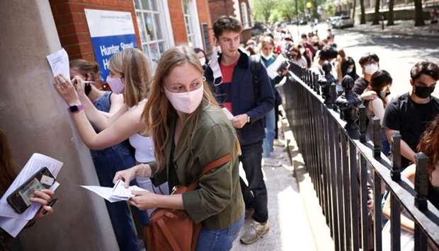 People fill in paperwork while queueing outside a vaccination centre for young people and students at the Hunter Street Health Centre in London