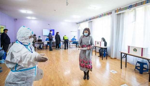 An election worker wearing a protective suit amid the Covid-19 coronavirus pandemic gestures to a woman voting at a polling site in Ulaanbaatar, the capital of Mongolia