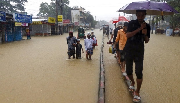 People wade along a road in a flooded area following heavy monsoon rainfalls in Sylhet on June 18, 2022.