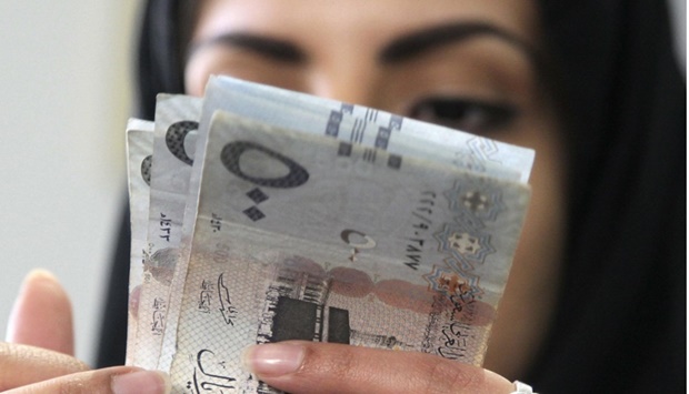 A Saudi woman counts riyal banknotes at a money exchange shop in Riyadh. Twelve-month forward contracts on Saudi Arabiau2019s riyal have plunged, a sign of confidence in the system used to keep the currency pegged to the dollar.