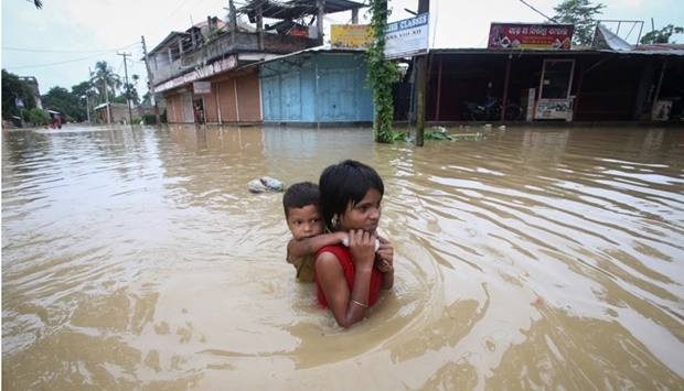 A girl carries her brother as she wades through a flooded road after heavy rains, on the outskirts of Agartala, India, June 18. REUTERS