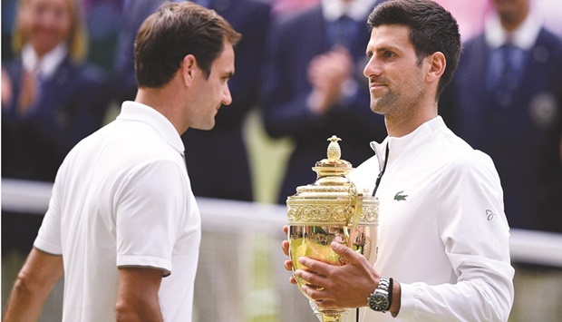 In this file photo taken on July 14, 2019, Serbiau2019s Novak Djokovic (right) holds the winneru2019s trophy and passes runner-up Switzerlandu2019s Roger Federer during the presentation at the end of the menu2019s singles final of the 2019 Wimbledon Championships at The All England Lawn Tennis Club in Wimbledon,  southwest London. (AFP)