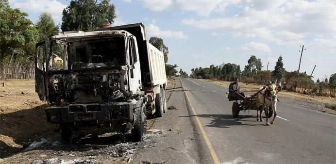 A man drives a horse-cart past the wreckage of a truck torched during demonstrations 