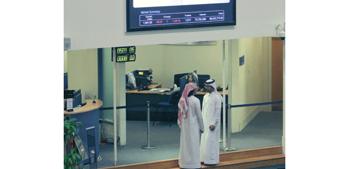Two Emirati investors talk under a screen board at the Dubai Financial Market