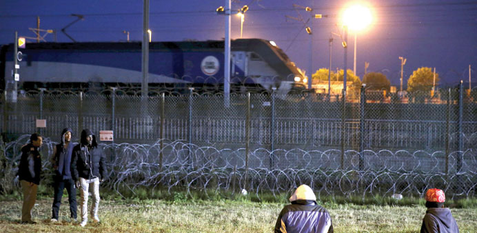 Migrants wait near a fence with razor barbs as an Eurotunnel freight shuttle goes to England by Channel Tunnel in Calais, late on Sunday.