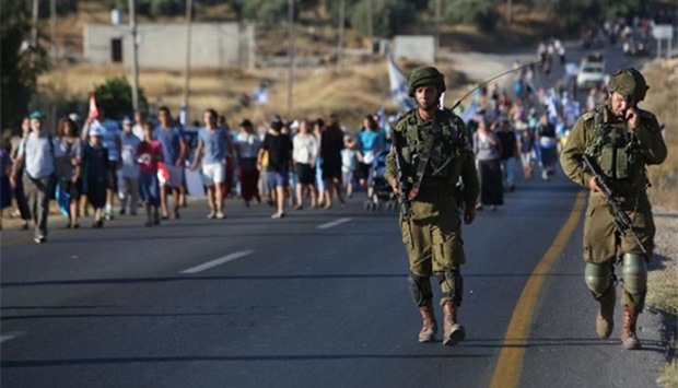 Israeli soldiers watch as hundreds of settlers march between the Palestinian village of Tarama and the Israeli settlement of Otniel, south of Hebron in the occupied West Bank, demanding more security for settlements following a wave of deadly attacks by Palestinians.